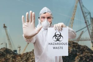 Technician in coverall warns about hazardous waste in a landfill instead of recycle center.